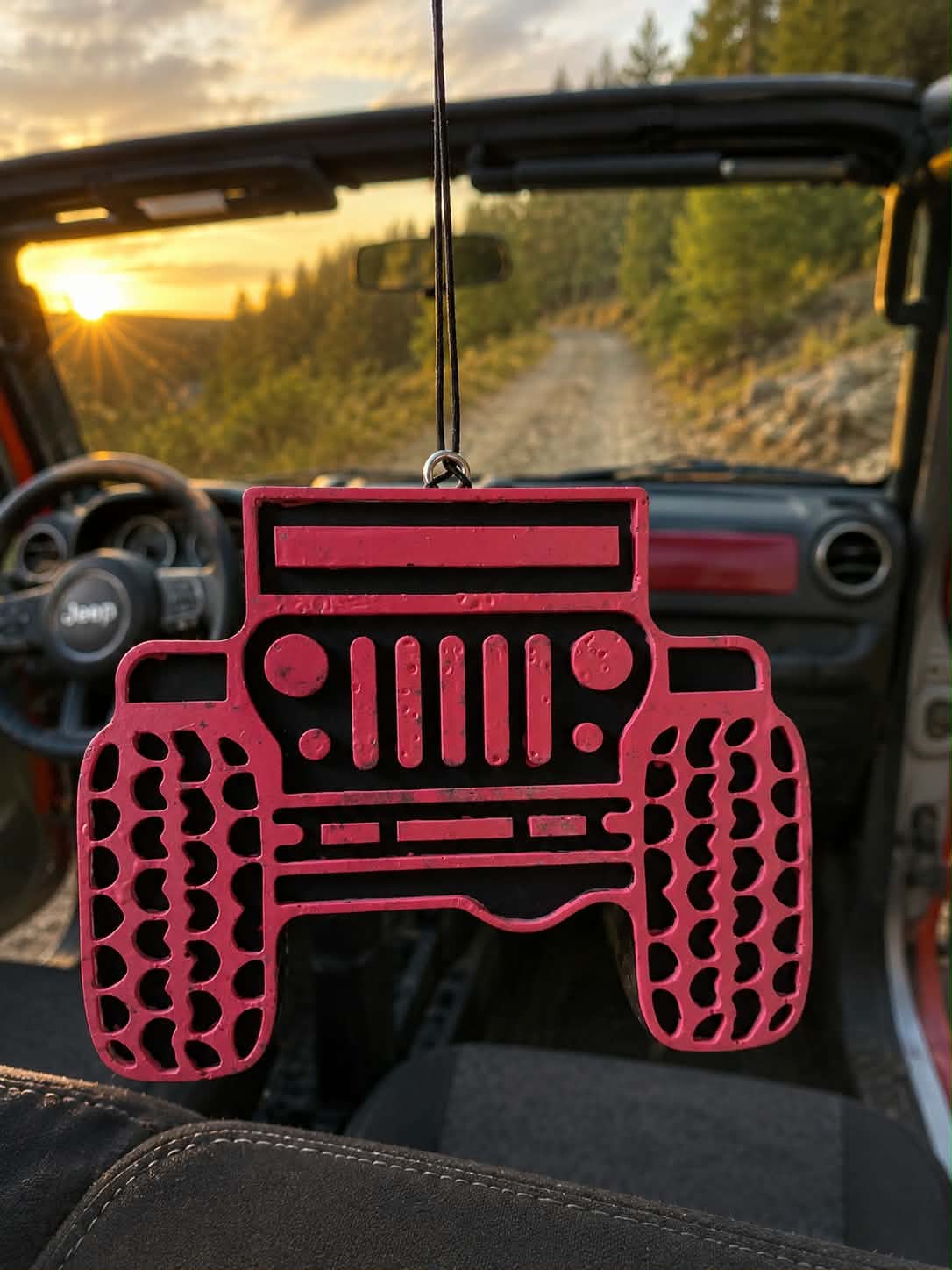 Pink Trail Rig Jeep-shaped car freshie hanging inside a Jeep at sunset on a dirt trail